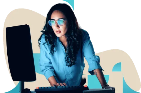 Professional with long dark hair in blue top working at computer desk wearing glasses