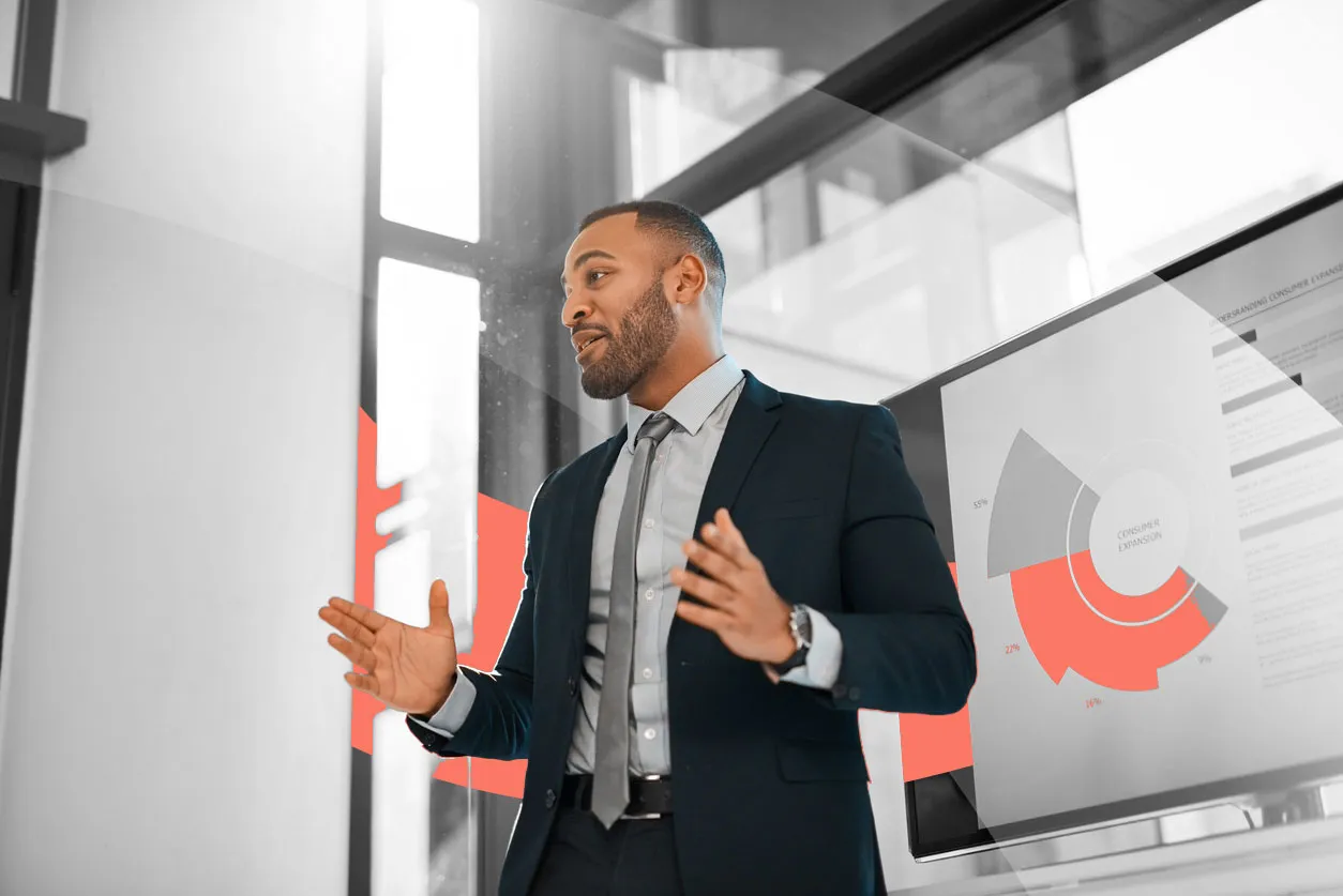 Business professional giving a presentation in an office, explaining data shown on a screen with charts and graphs.