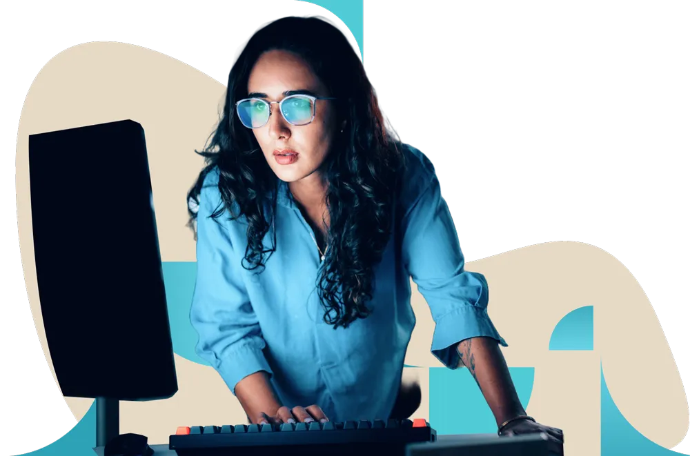 Professional with long dark hair in blue top working at computer desk wearing glasses