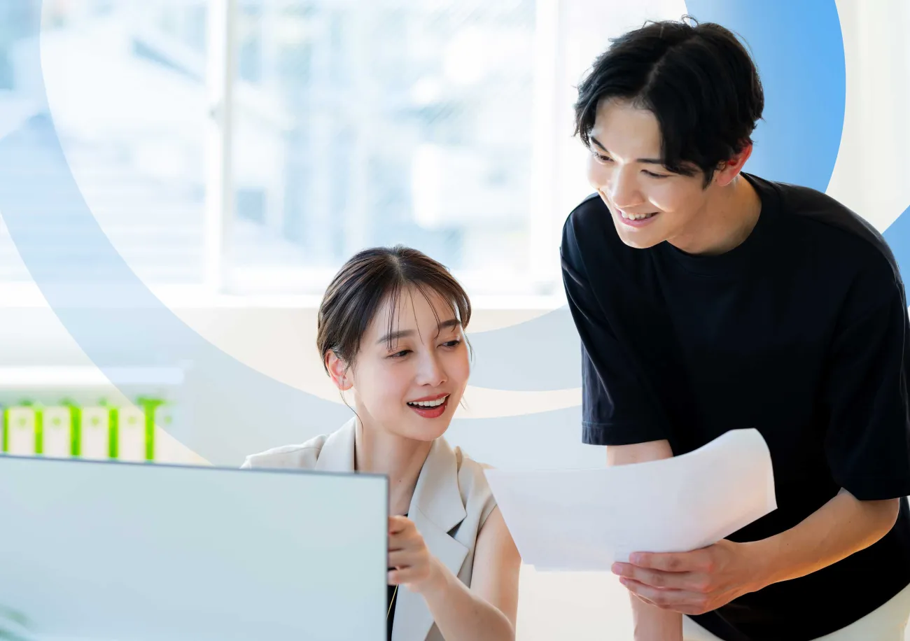 Two co-workers reviewing printed documents together at a computer