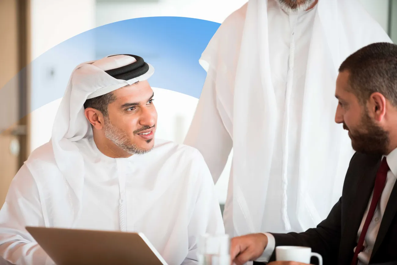 Businessman in traditional Middle Eastern attire meeting with a colleague and discussing work over coffee and a laptop.