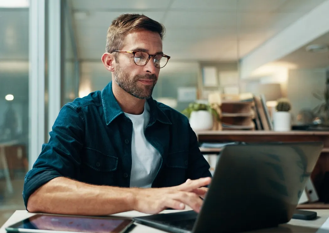 Hombre con gafas trabajando en una computadora portátil en una oficina luminosa