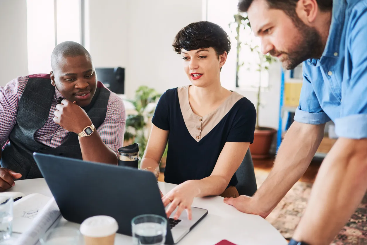 Three colleagues collaborating at a desk with a laptop in an office