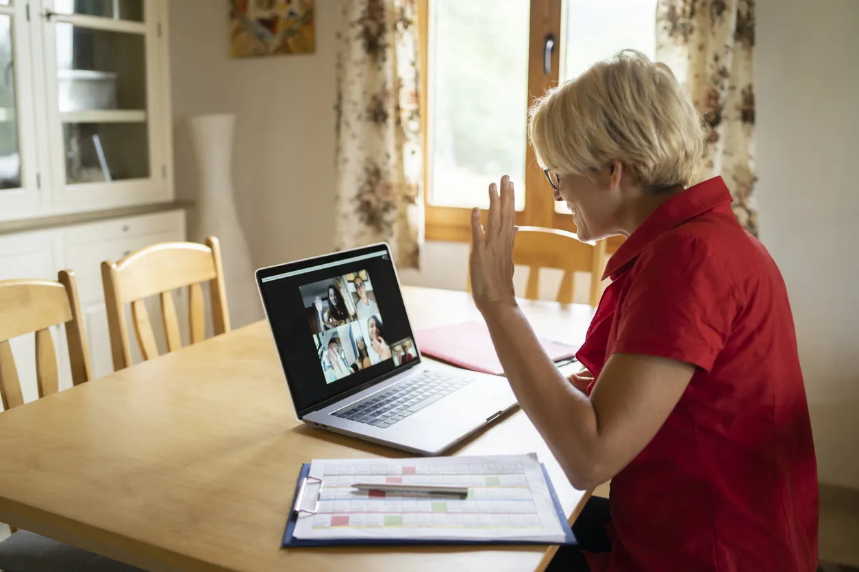 Senior woman video calling on laptop at dining table in cozy room