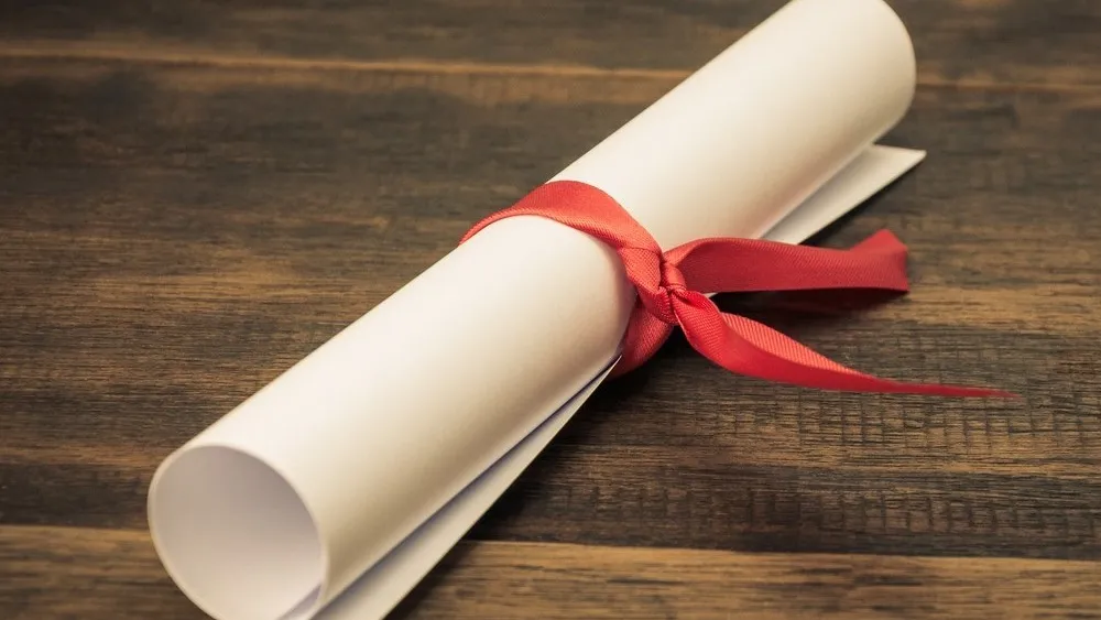 Rolled paper scroll tied with red ribbon on dark wooden surface