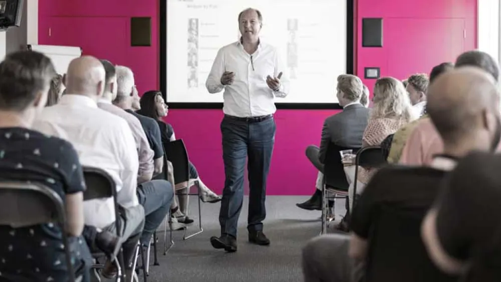 Man in a white shirt strolling through the centre column of a busy of classroom