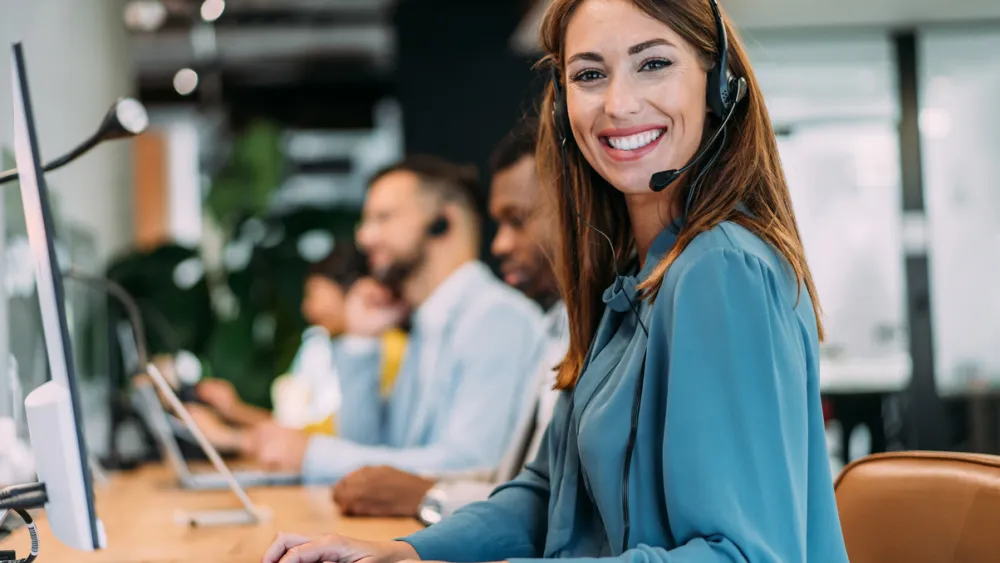 Customer service representative in blue blosue with headset working at computer in office setting