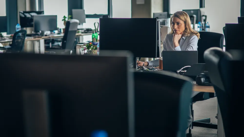 A woman working on a laptop in a spacious office with multiple desks and monitors