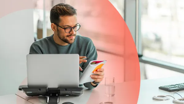 Professional working at a desk with a laptop and notebook and reviewing notes in a notebook.