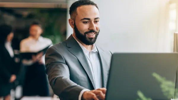 Professional in grey suit working on laptop at standing desk in bright office space